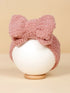 Pink textured headband with a large bow, displayed on a white round stand against a neutral background.