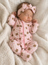 Newborn girl sleeping in a pink checkered onesie with teddy bear designs, wearing a matching headband.