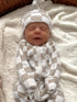 Newborn baby in a beige and white checkered outfit, peacefully sleeping on a soft blanket.