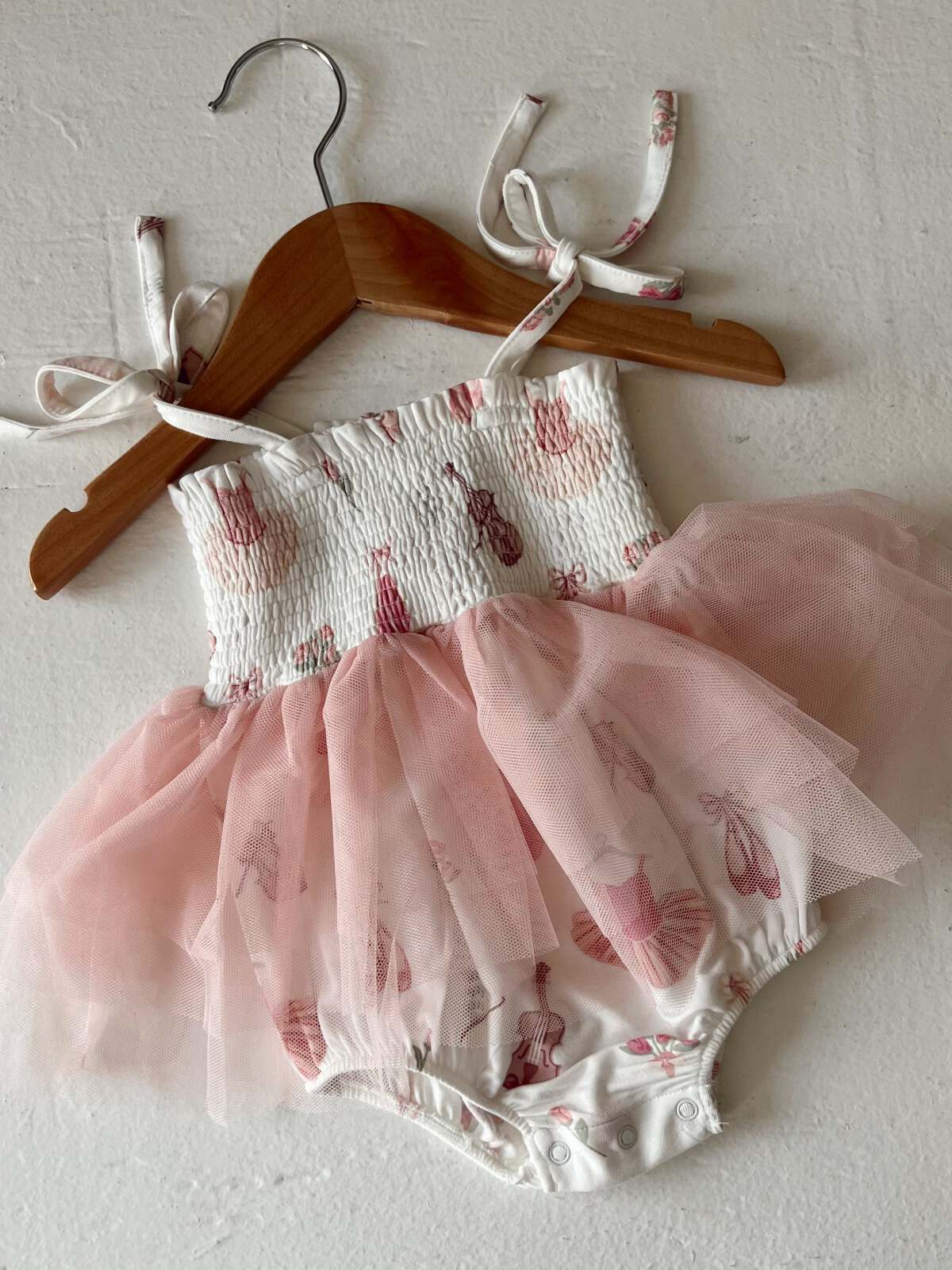 Baby dress with pink tulle skirt and ballet print, hanging on a wooden hanger against a white background.