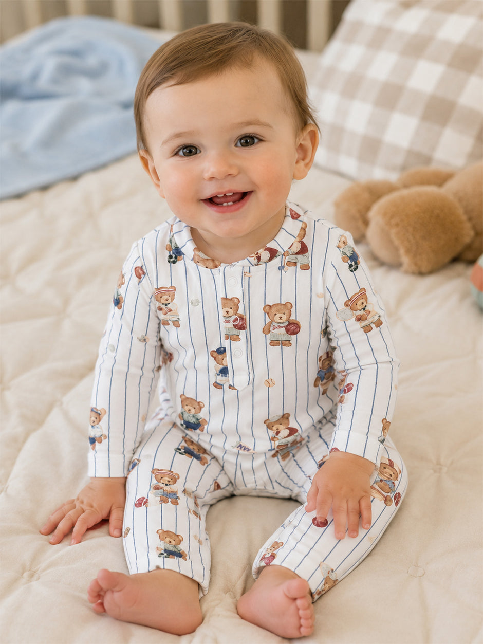 Smiling toddler in a bear-patterned outfit sits on a bed, surrounded by soft toys, radiating joy and innocence.
