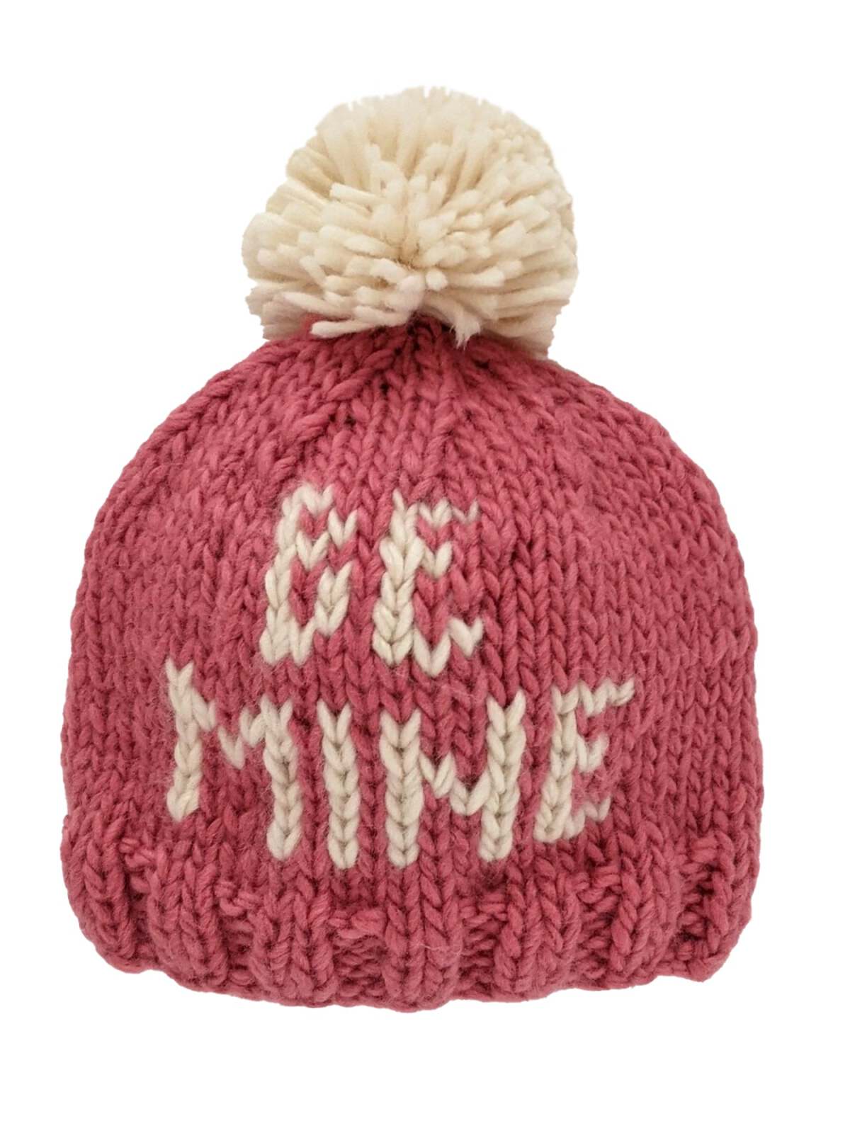 Knitted pink winter hat with white pom-pom and the text "BE MINE" on the front.