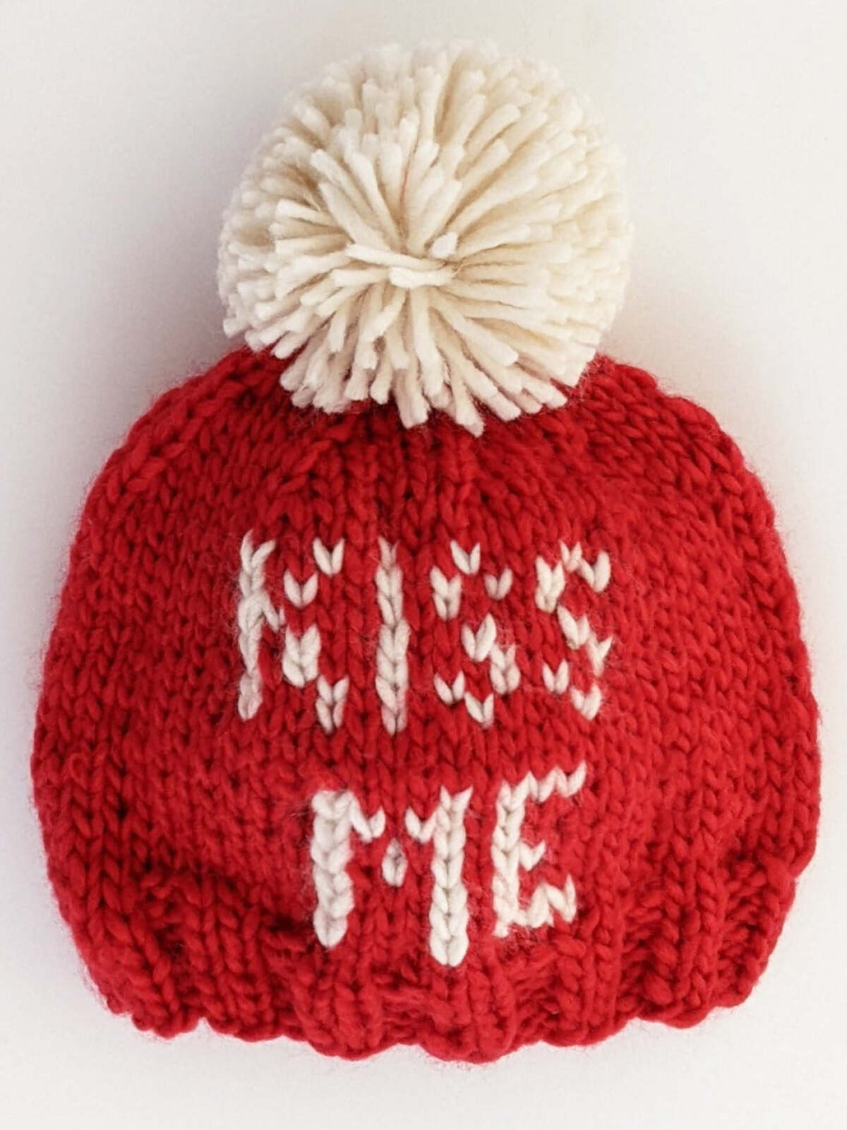 Red knitted hat with a white pom-pom, featuring the text "KISS ME" in white letters.