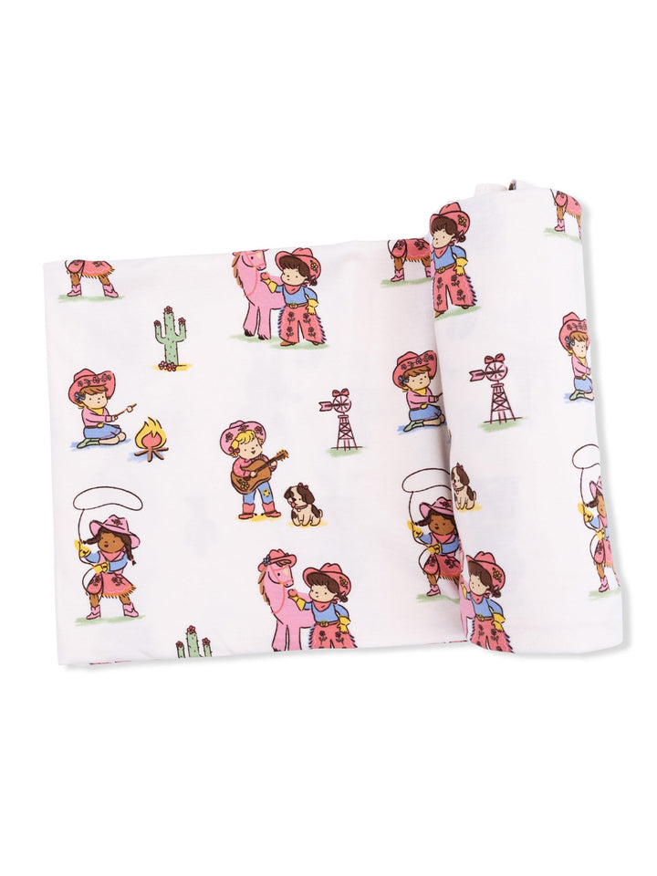 Colorful fabric featuring playful cowgirl illustrations with animals, musical instruments, and desert elements.