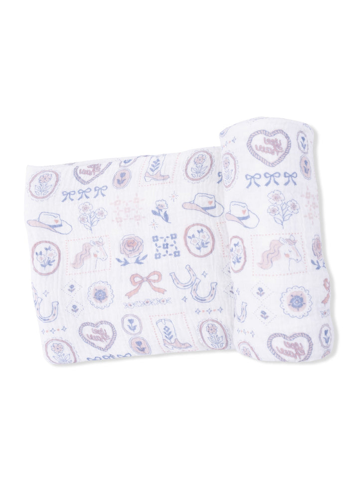 Whimsical muslin blanket featuring playful cowboy and floral designs in pastel colors.