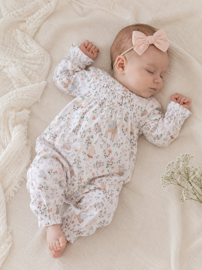 Sleeping baby in a floral onesie with a pink bow, resting on a soft blanket with delicate flowers nearby.