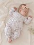 Sleeping baby in a floral onesie with a pink bow, resting on a soft blanket with delicate flowers nearby.