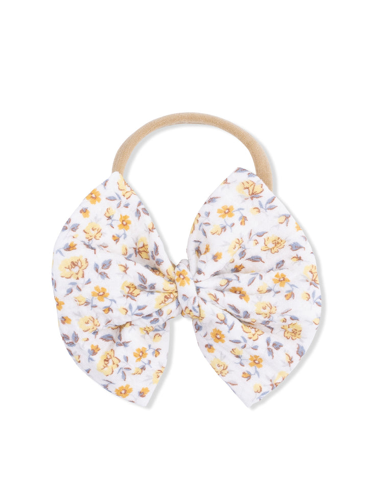 Floral fabric hair bow on a beige elastic band, featuring yellow flowers on a white background.