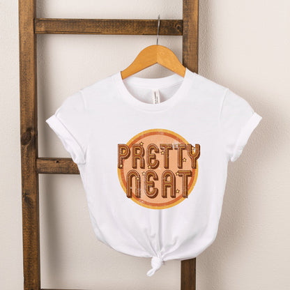 White t-shirt with "Pretty Neat" text design, displayed on a wooden rack against a beige wall.