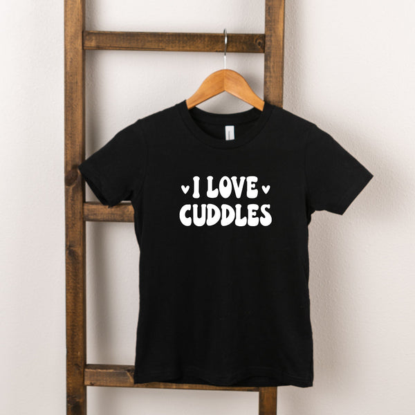 Black t-shirt hanging on a wooden ladder with the text "I LOVE CUDDLES" printed in white.
