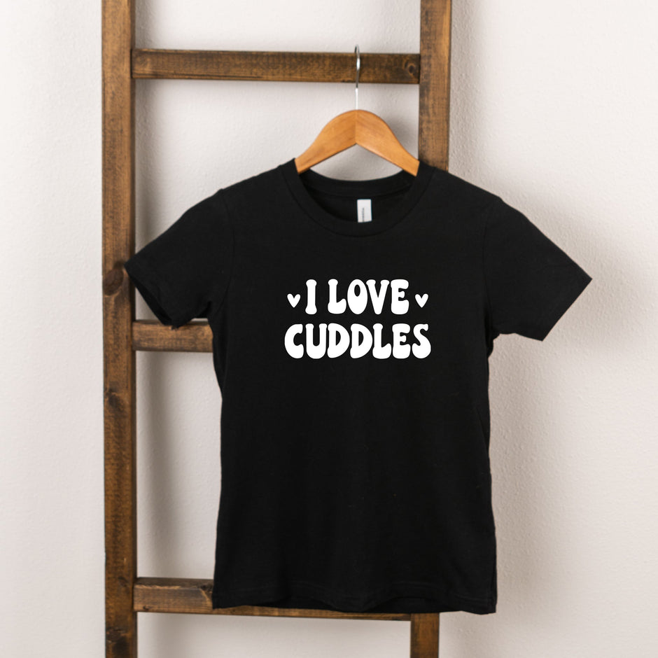 Black t-shirt hanging on a wooden ladder with the text "I LOVE CUDDLES" printed in white.
