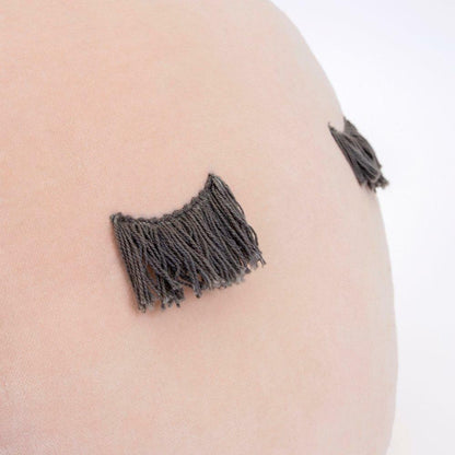 Close-up of a soft, round pillow featuring decorative dark fringe accents on a light background.