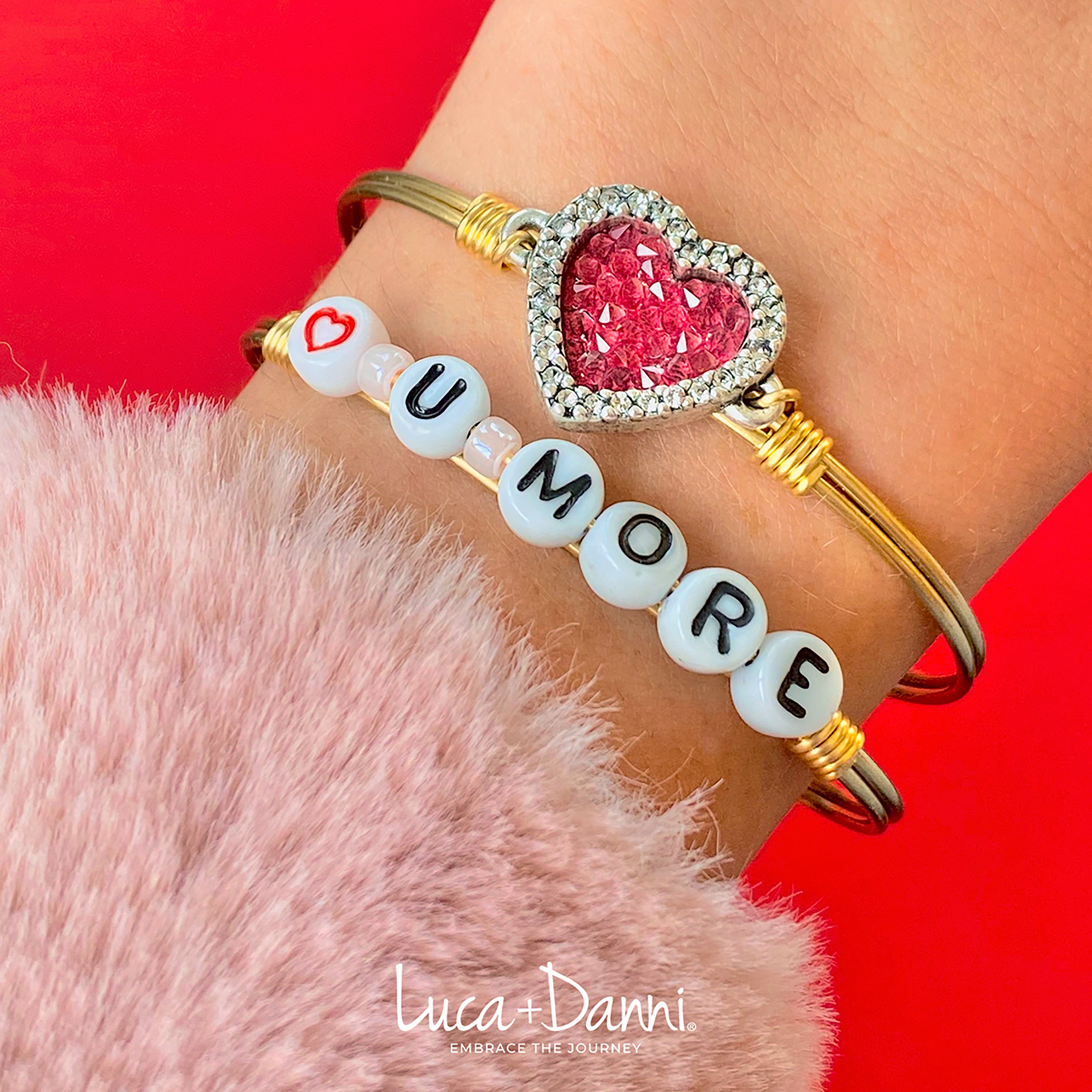 Two bracelets on a wrist: one with a sparkling heart charm, the other spells "I LOVE U MORE" in beads.
