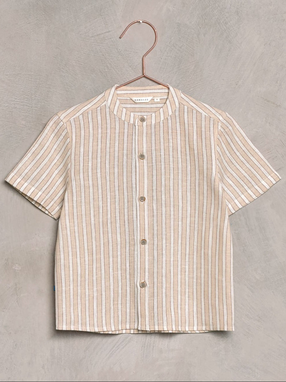 Short-sleeve striped linen shirt with a round collar, hanging on a copper hanger against a textured background.