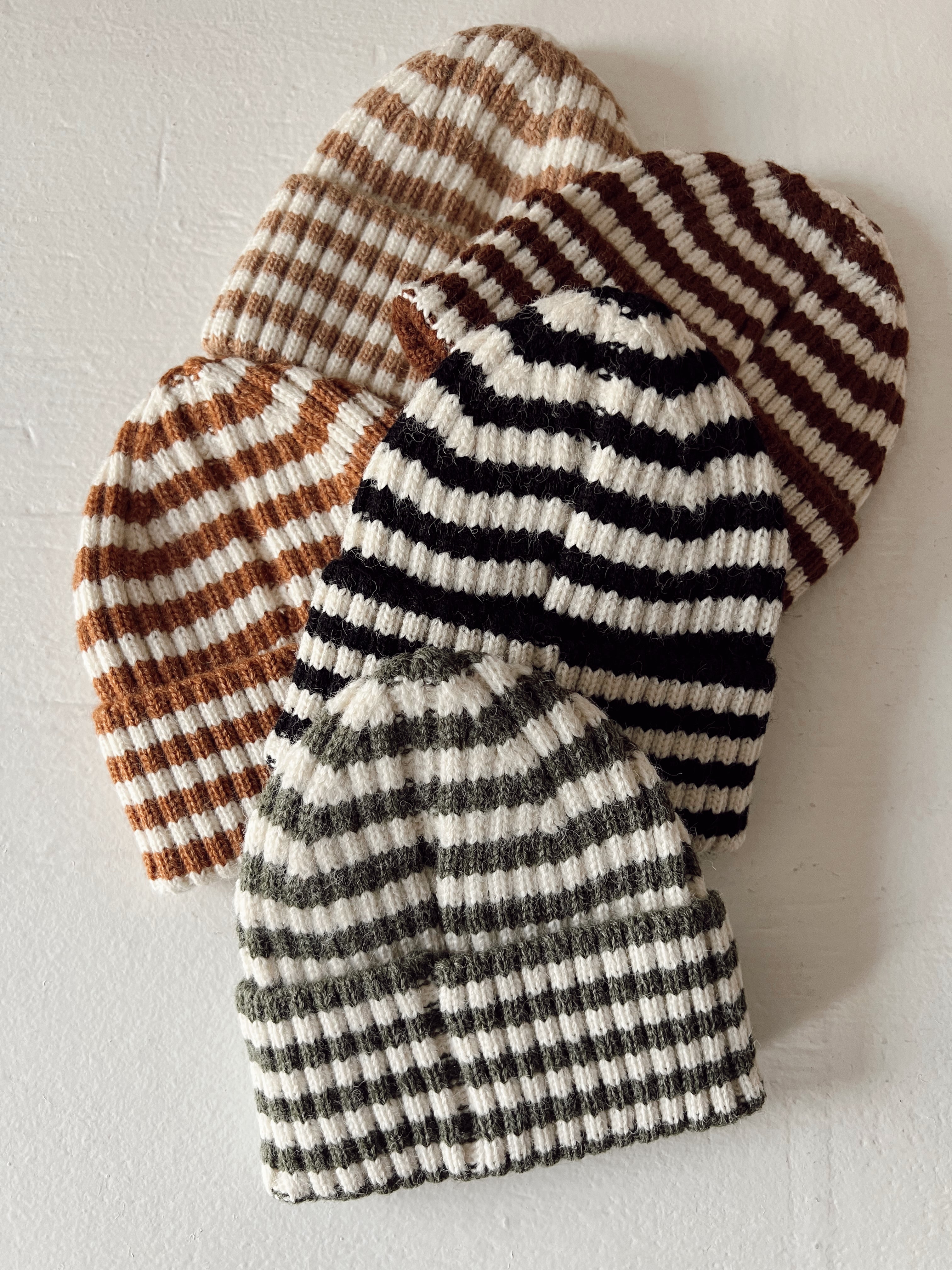 Four striped beanie hats in brown, black, and green arranged on a light background.