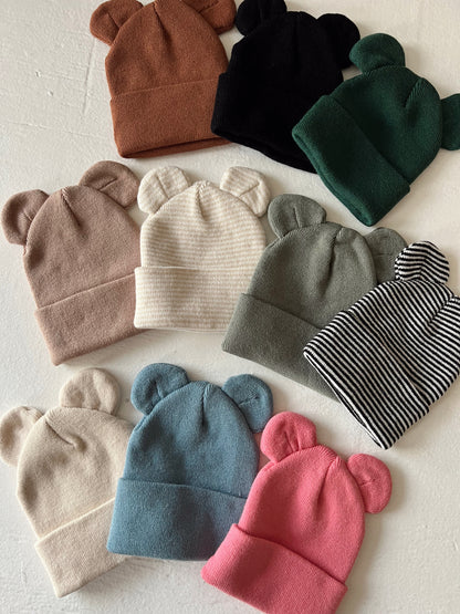 Colorful baby beanies with bear ears, arranged in a flat lay on a light background.