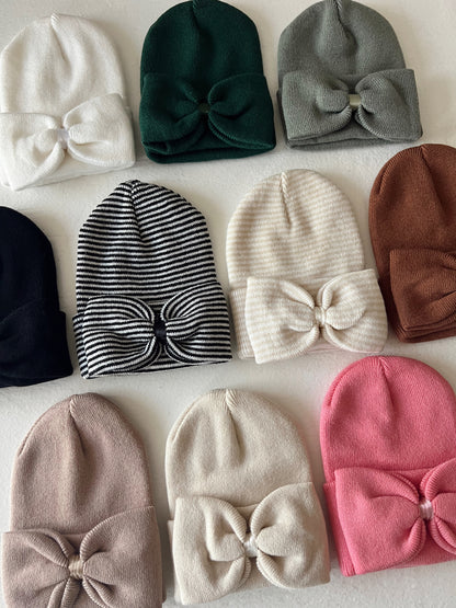 Assorted beanie hats with bows in various colors and patterns on a light background.