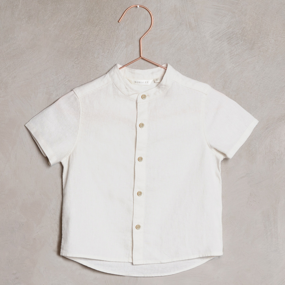 Short-sleeve white button-up shirt hanging on a copper hanger against a textured background.