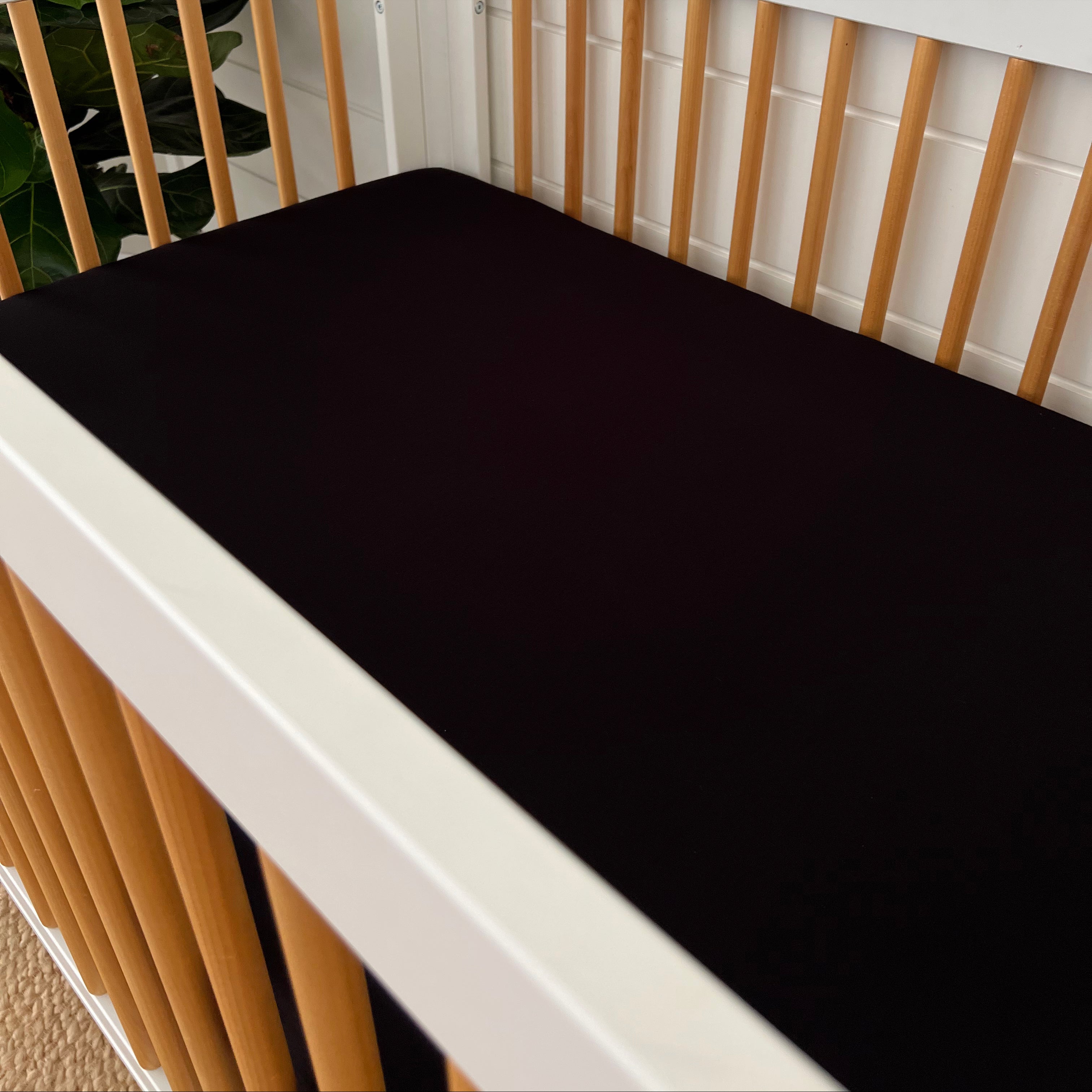 Black crib mattress in a modern crib with wooden slats and a floral background.