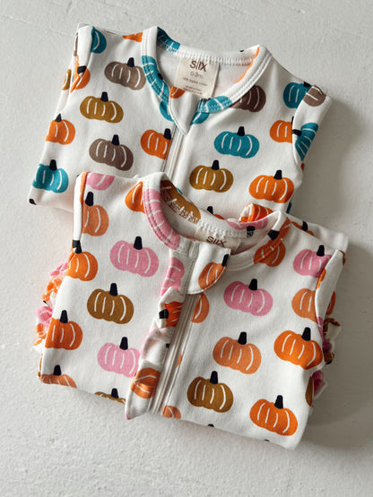 Two baby outfits featuring colorful pumpkin patterns on a white background, laid flat on a light surface.