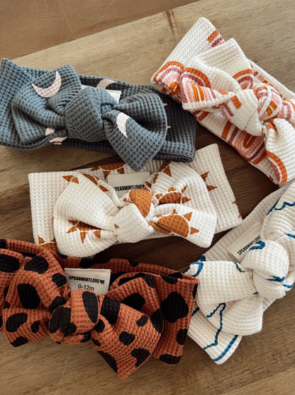 Five colorful baby headbands with various patterns on a wooden surface.