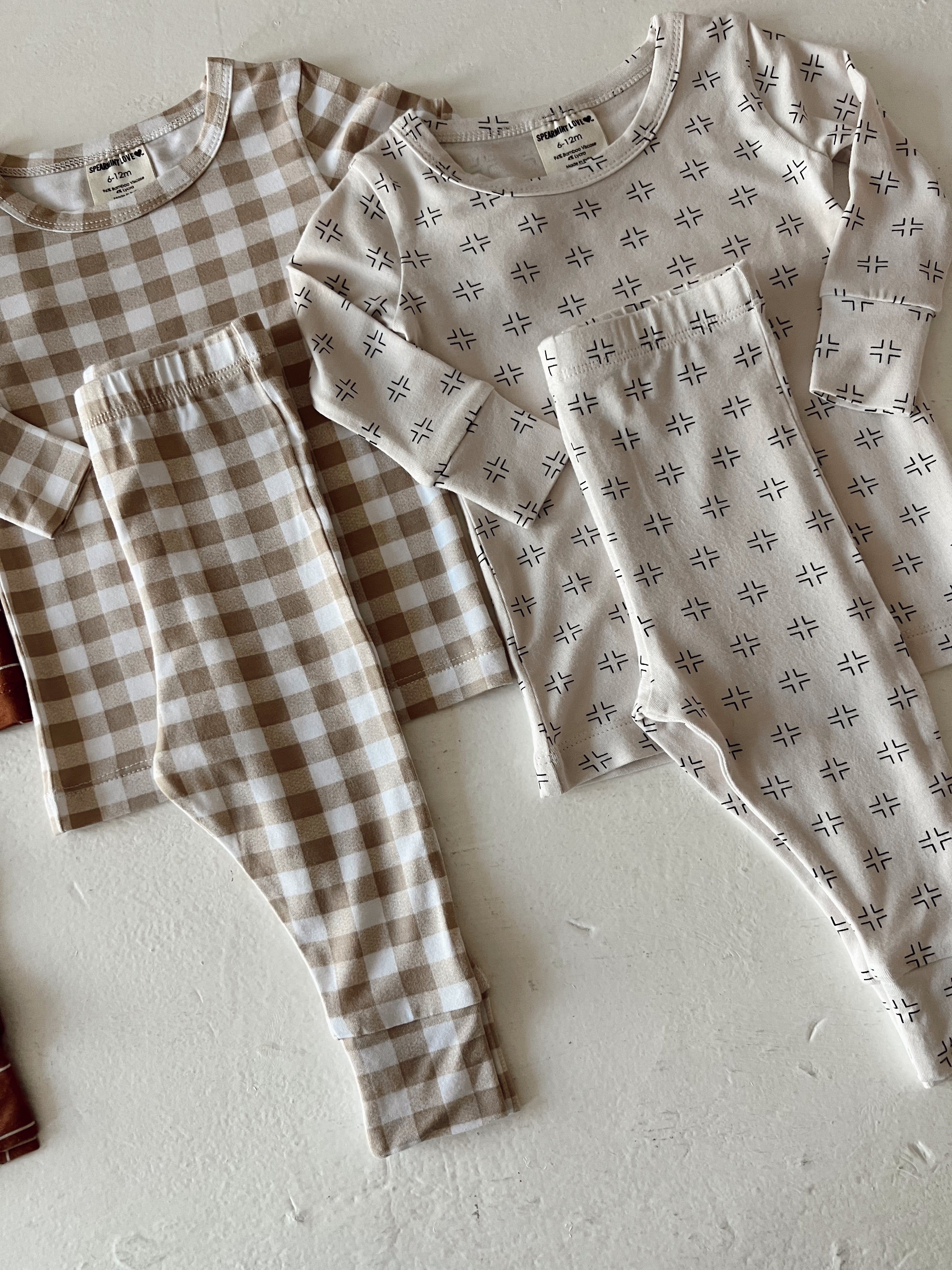 Two sets of matching children's pajamas in neutral colors and patterns, laid out on a textured surface.