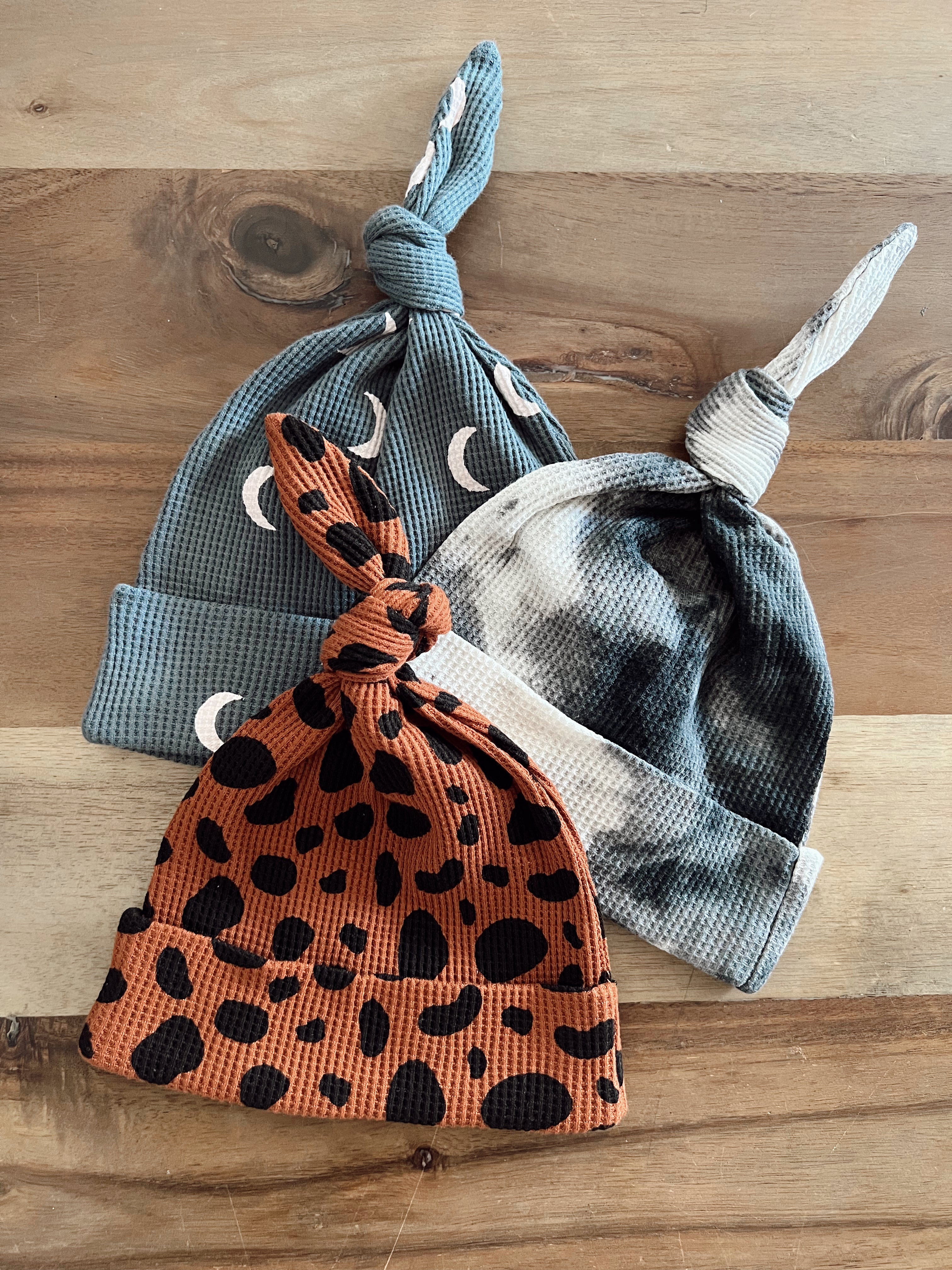 Three distinct baby hats in various colors and patterns, displayed on a wooden surface.