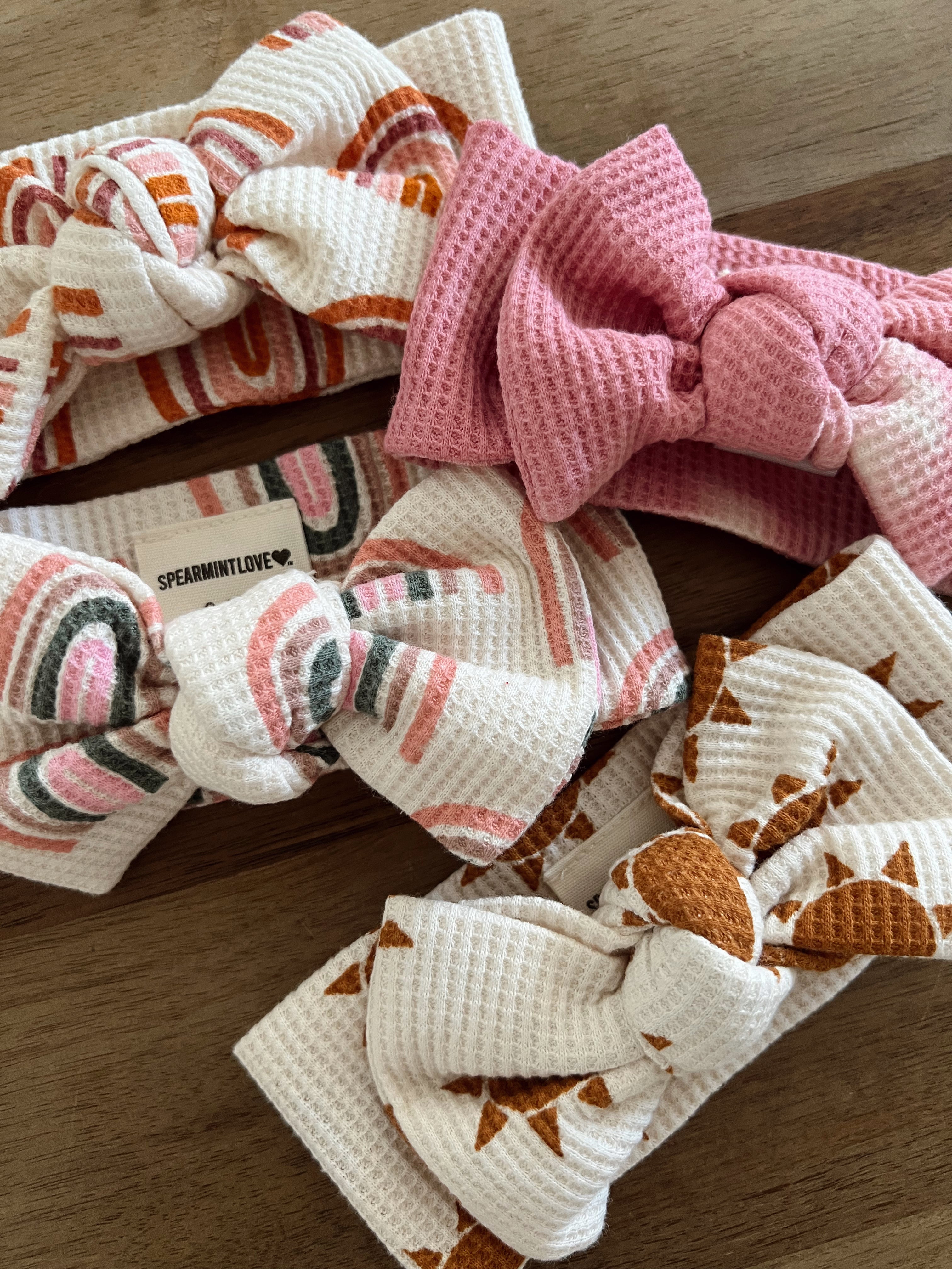 Four uniquely patterned headbands with bows laid on a wooden surface, showcasing various colors and textures.