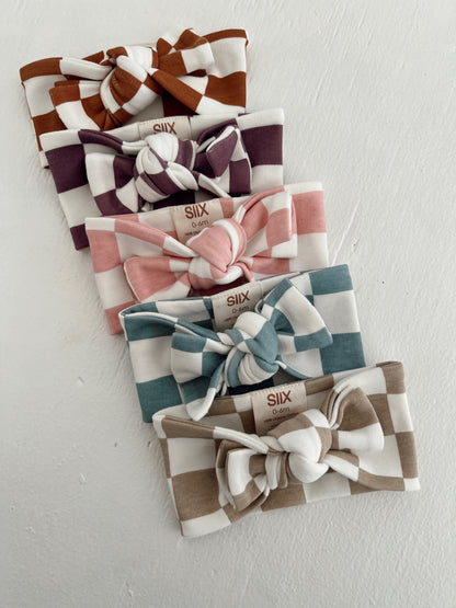 Five checked headbands in various colors arranged neatly, featuring bows and size tags.