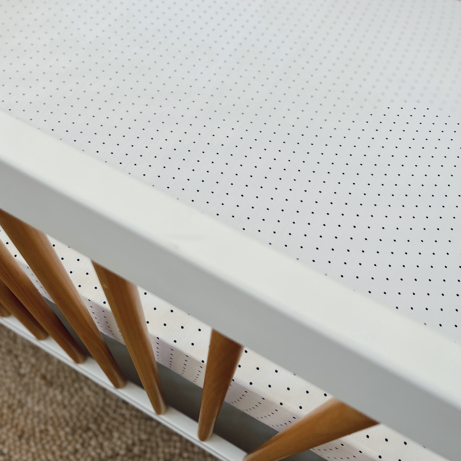 Top view of a white crib featuring a dotted bedding pattern and wooden slats.
