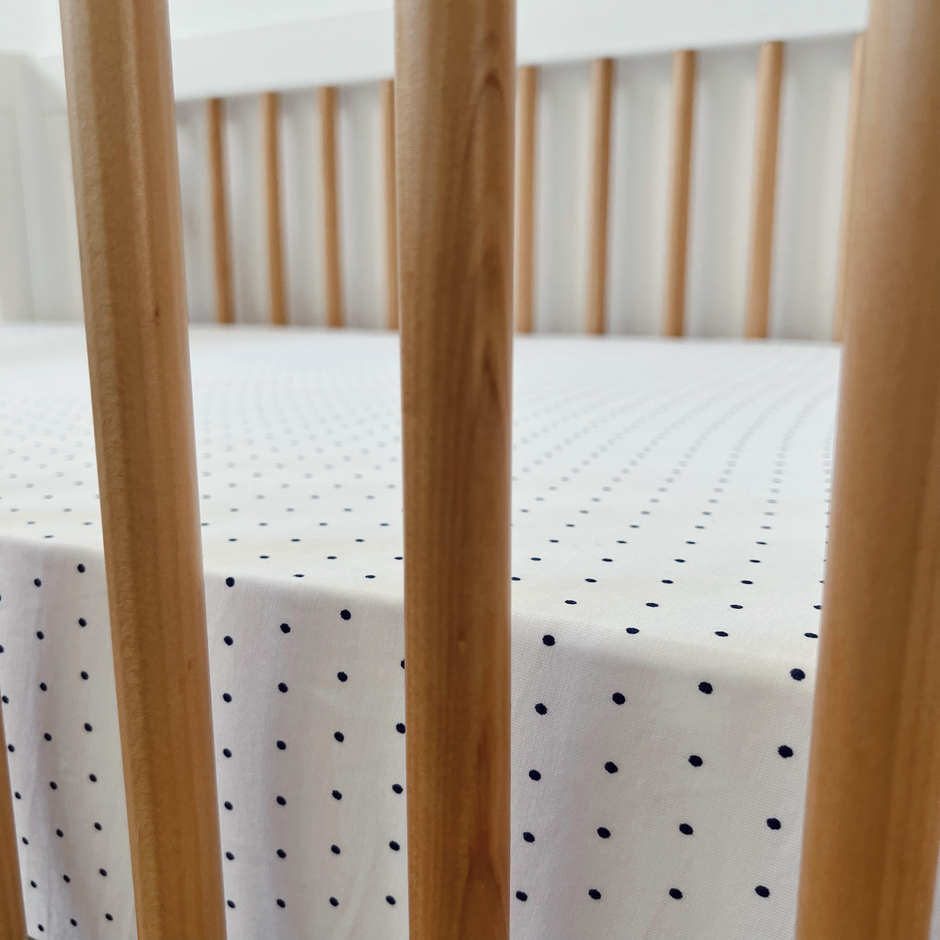 Close-up of a crib's wooden slats and a white fitted sheet with navy polka dots.