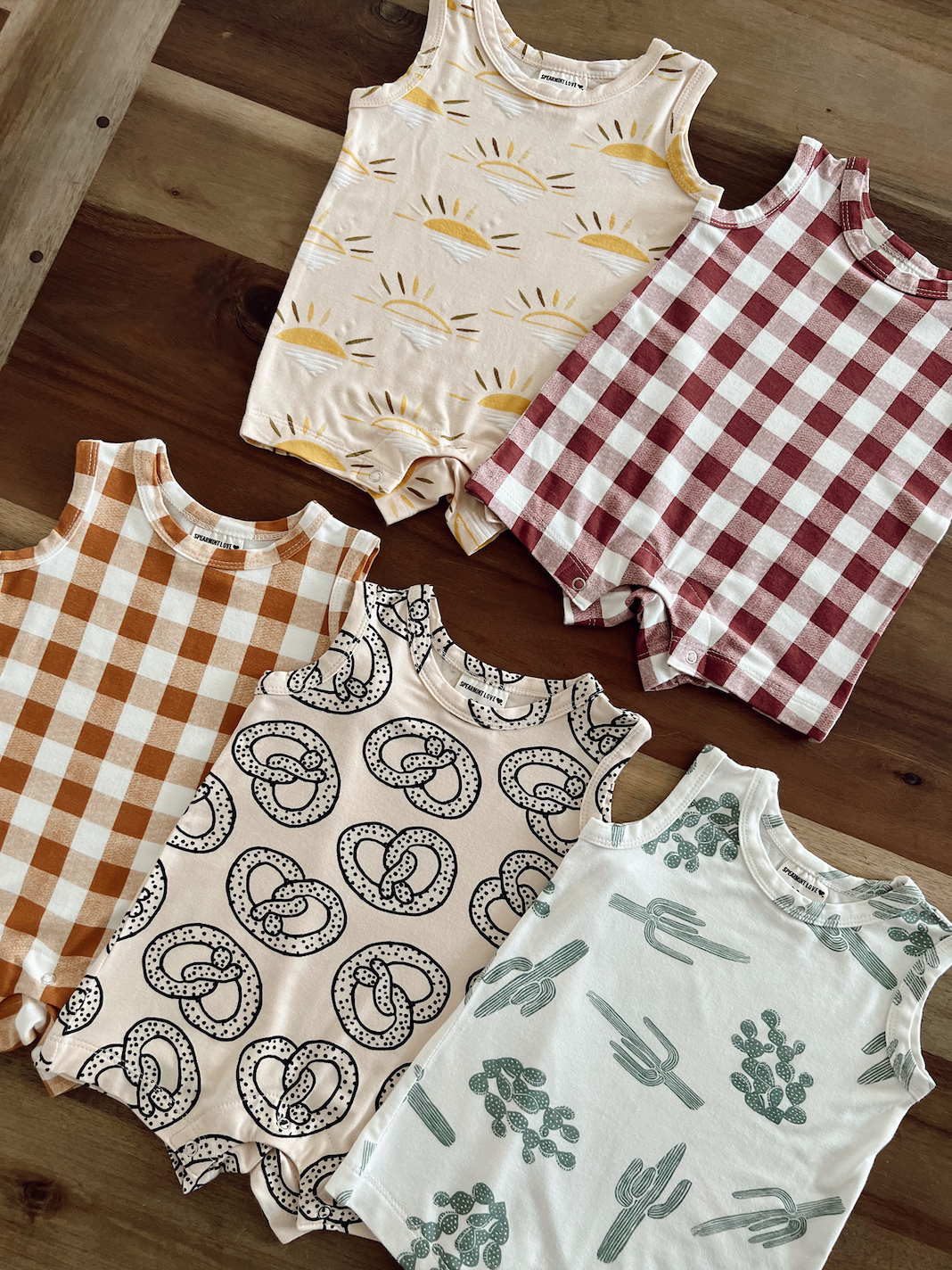 Six toddler onesies with various designs: sun, checker, pretzel, and cactus patterns on a wooden surface.